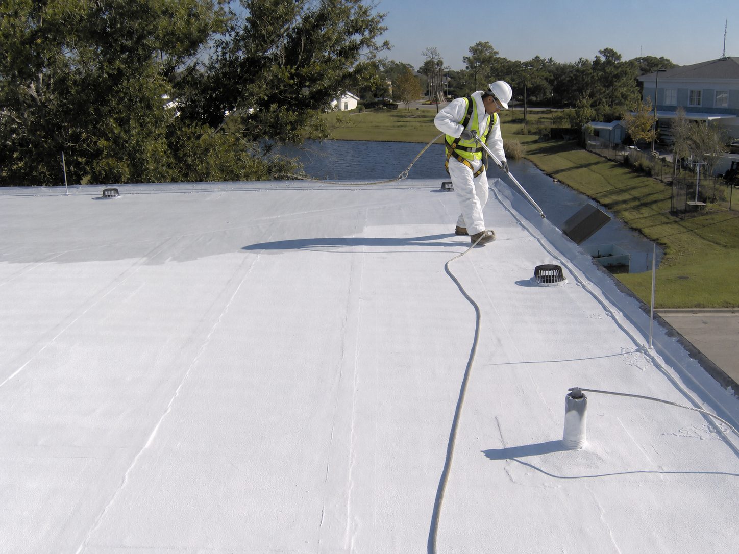 Technicien appliquant une peinture réfléchissante thermique sur une toiture de bâtiment professionnel
